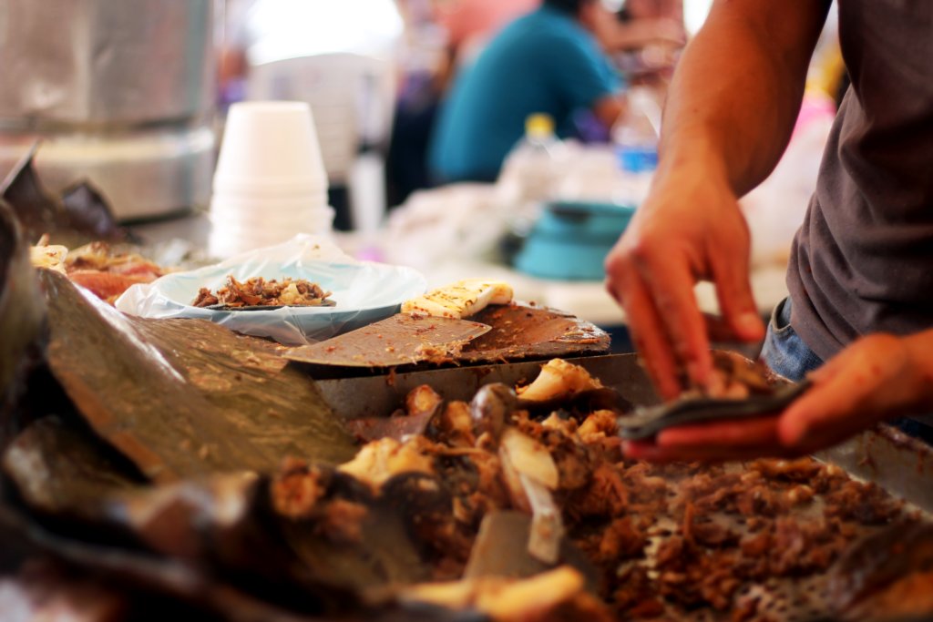 Cocinero picando y sirviendo tacos de barbacoa recién salidos del horno de tierra